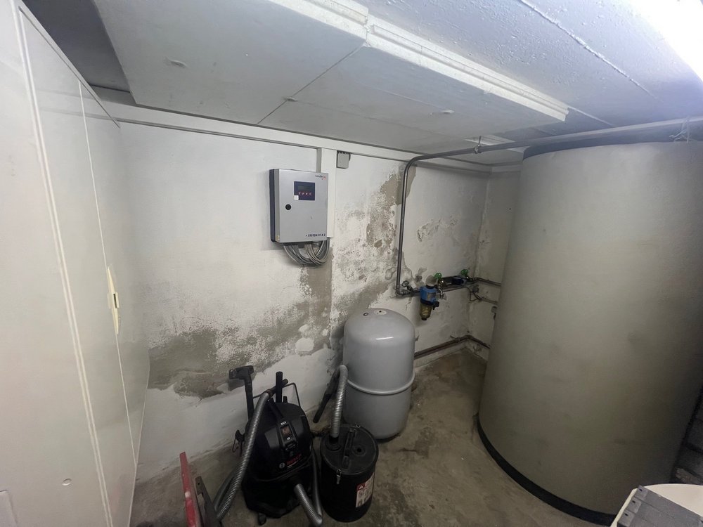 Feuchte Kellerwand mit Abplatzungen neben Technikbehältern