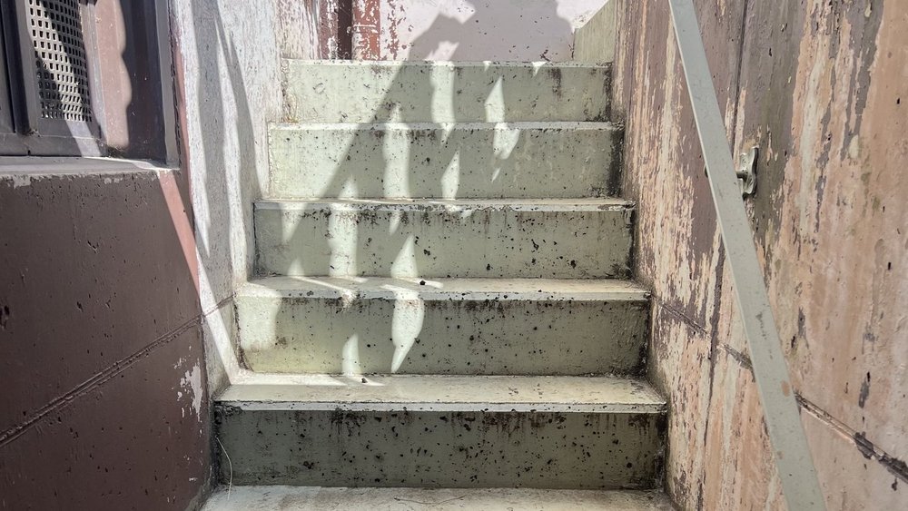 Betontreppe im schmalen Außengang mit dunklen Flecken und Metallgeländer