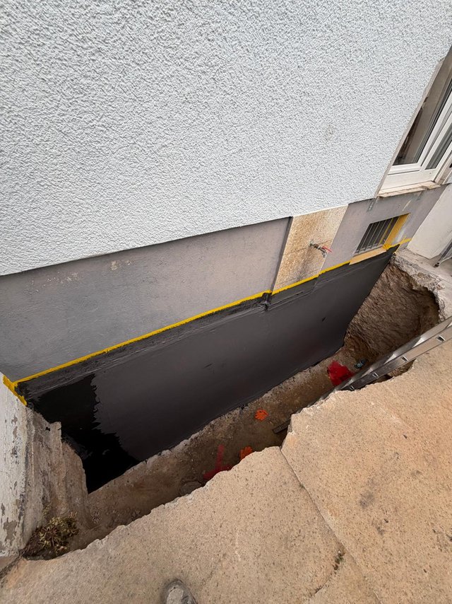 Schwarze Masse auf freigelegter Kellerwand neben Baugrube aufgetragen