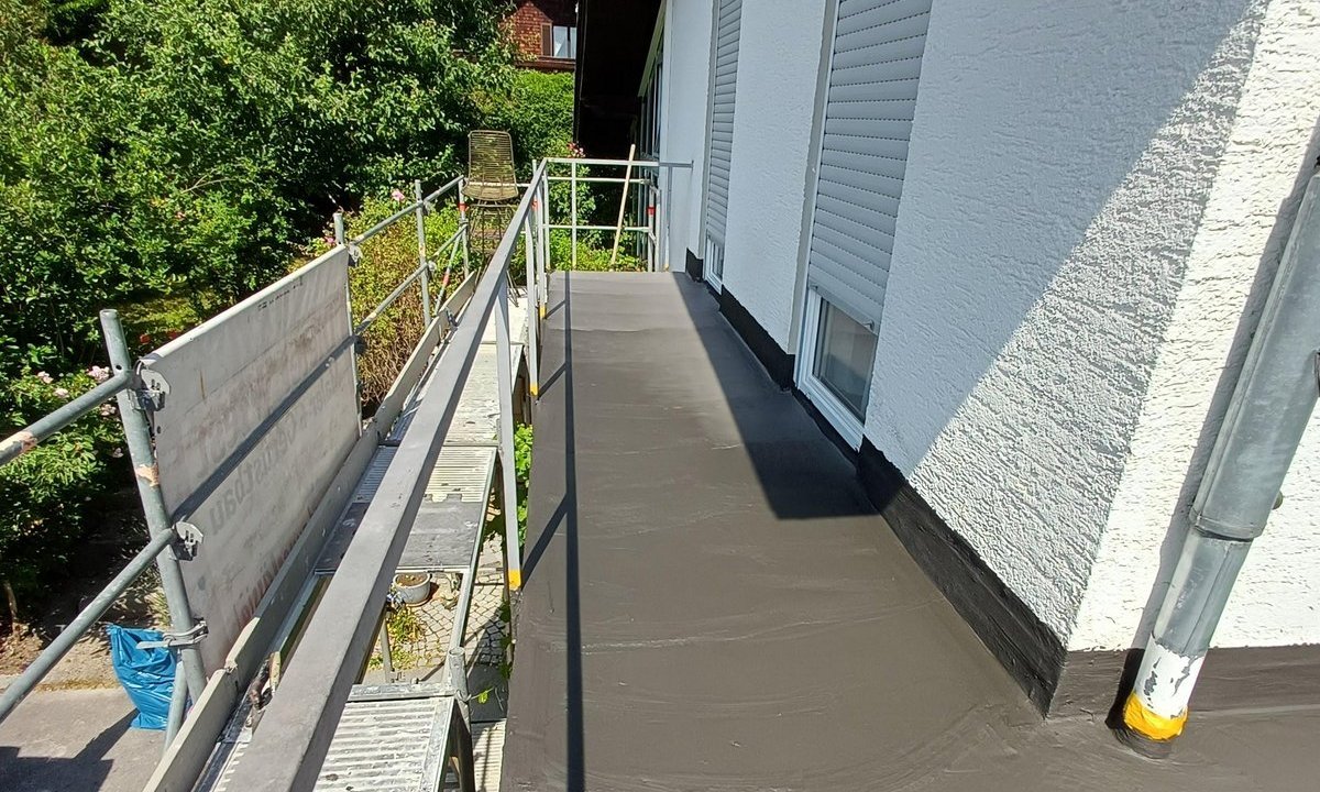 Balkon mit frisch aufgetragener schwarzer Masse, Geruest und weisse Fassade mit Rolllaeden