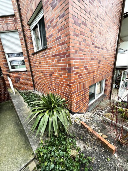 Roter Klinkerbau mit Fenster und bepflanztem Beet im Vordergrund