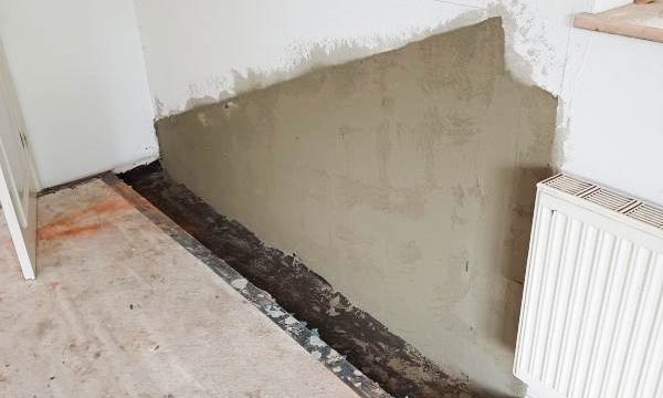 Graue Masse auf Wand im Heizkörperbereich, offener Bodenstreifen entlang der Wand