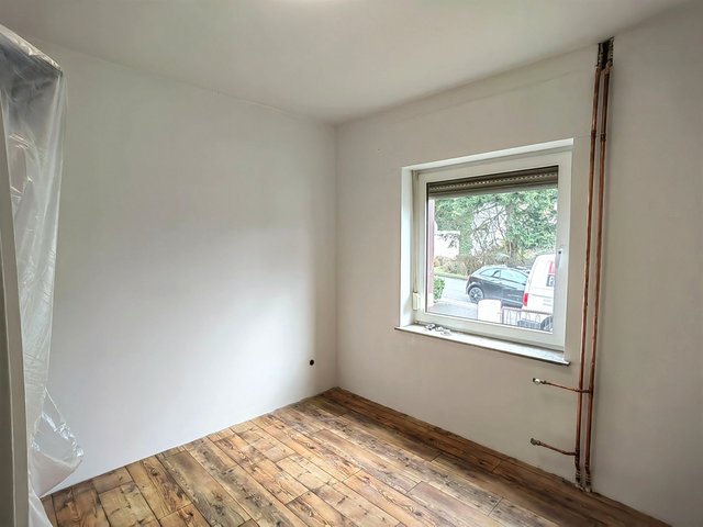 Leerer Raum mit Holzoptikboden, Fenster und freiliegenden Kupferrohren