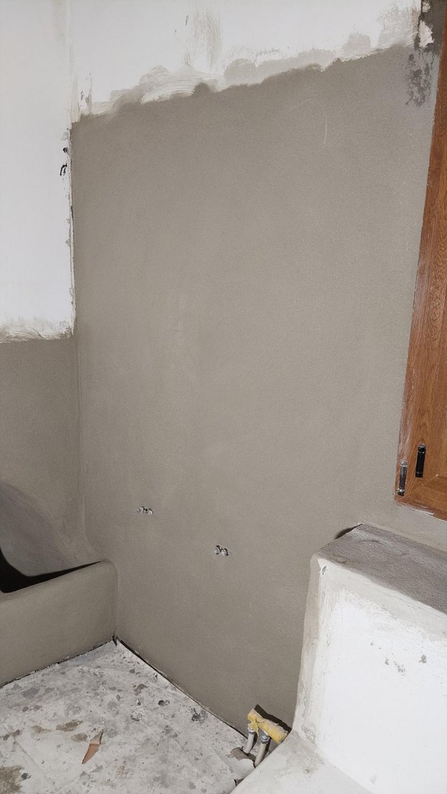 Graue Masse auf Kellerwand, Fenster rechts und freiliegende Leitungen am Boden