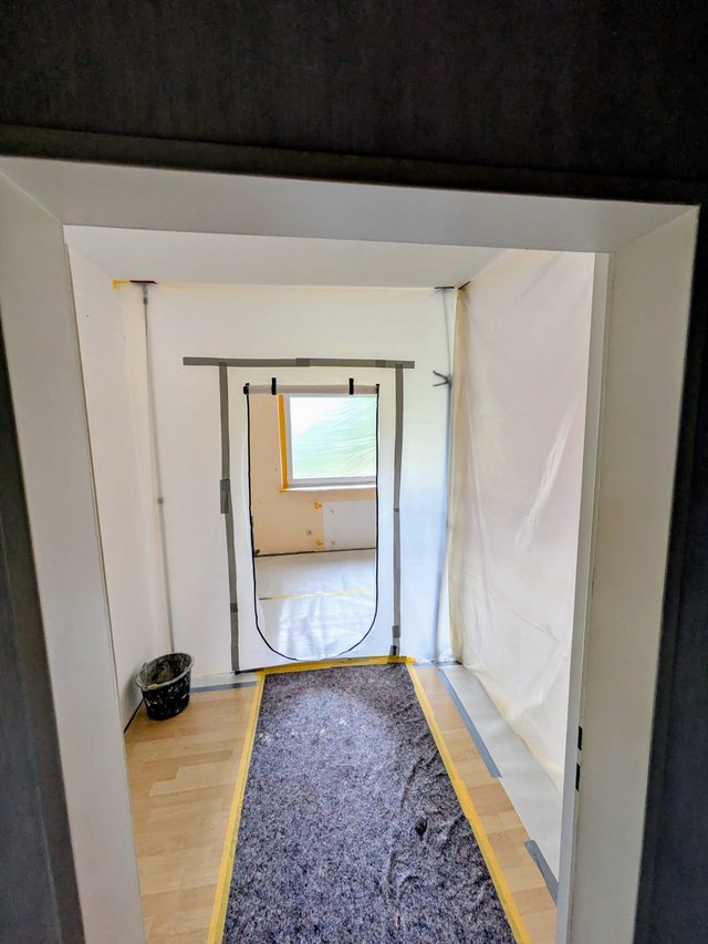 Abgeklebter Durchgang mit Folienwand und Staubschutztür in renoviertem Zimmer