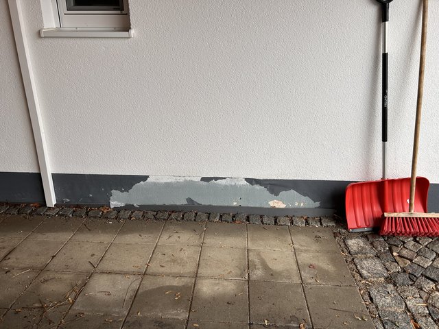 Abgeplatzte Beschichtung am Sockel eines Gebäudes über Pflastersteinen