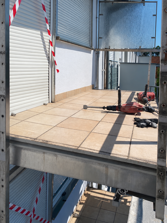 Fliesenbalkon mit Abbruchhammer, Bohrhammer und Arbeitshandschuhen auf Gerüst