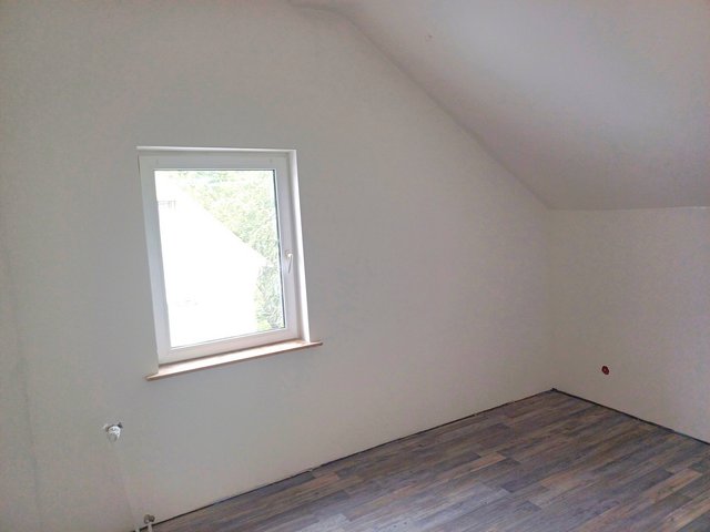 Helles Zimmer mit schräger Decke, Fenster und dunklem Holzfußboden