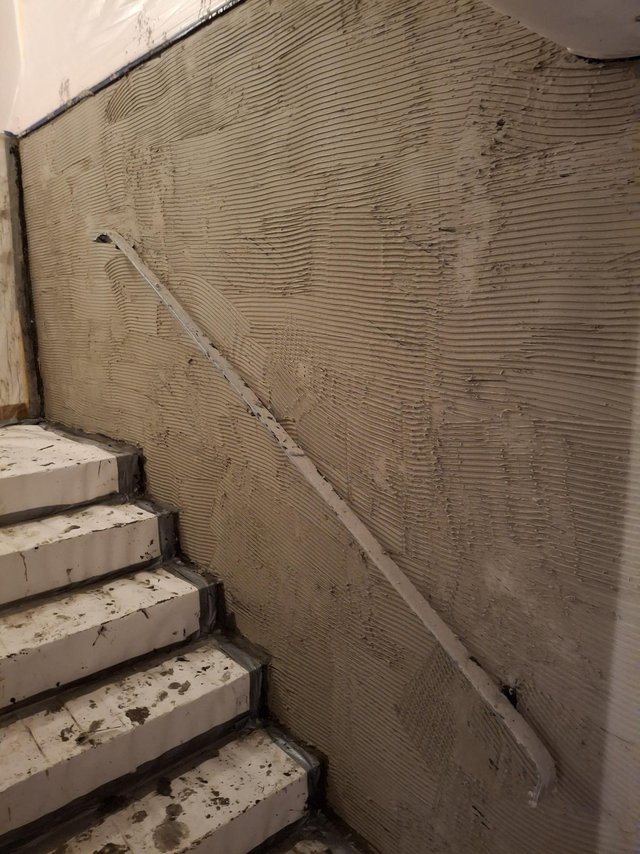 Graue Masse mit Zahnspachtelrillen an Treppenwand, unmontierte Handlaufleiste