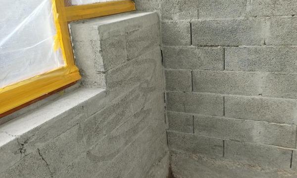 Abgeklebtes Fenster mit Folie neben grauer Betonsteinwand, Raum-Ecke.