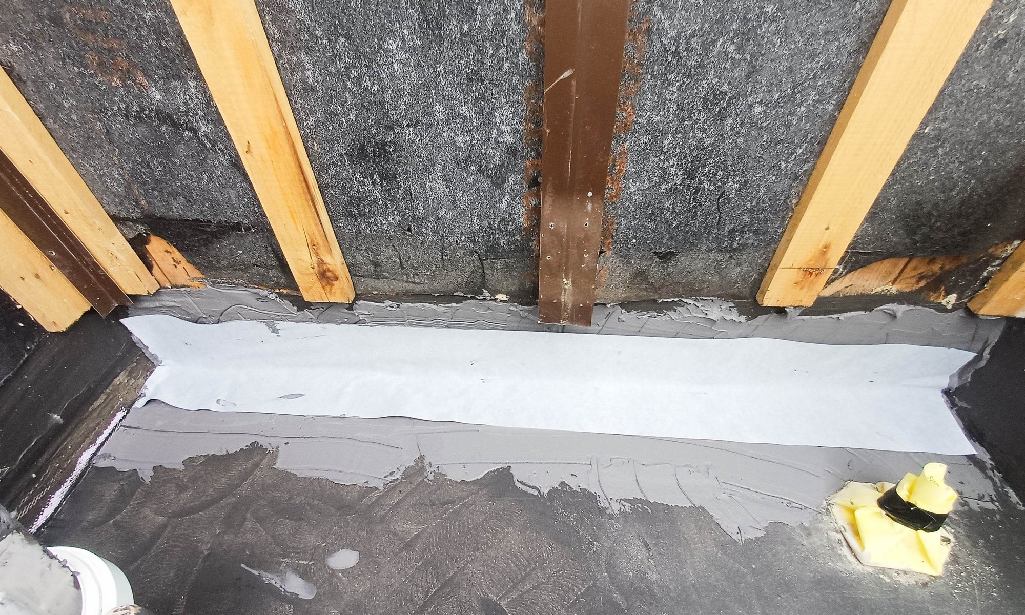 Helle Bahn liegt zwischen grauer Masse auf Bodenanschluss unter Holzbalken.