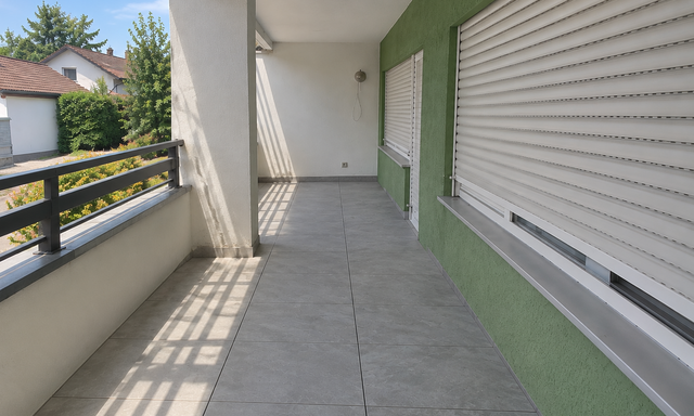 Leerer Balkon mit grauen Bodenfliesen, Metallgeländer und weißen Rollläden an grüner Wand