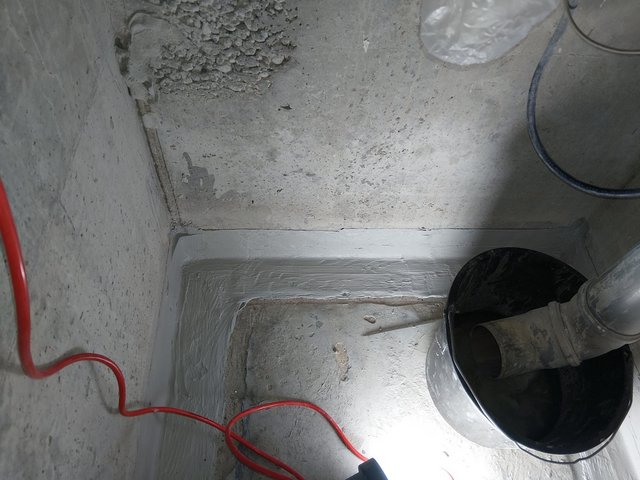 Abplatzende graue Schicht in Betonecke, Nahaufnahme mit Rohr und Eimer