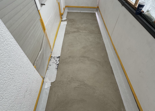 Frische graue Masse auf Balkonboden, Ränder sauber abgeklebt