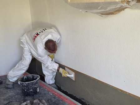 ISOTEC Mitarbeiter glättet graue Masse an Kellerwand.