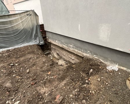 Freigelegte Fundamentwand mit offenem Erdaushub neben dem Gebäude