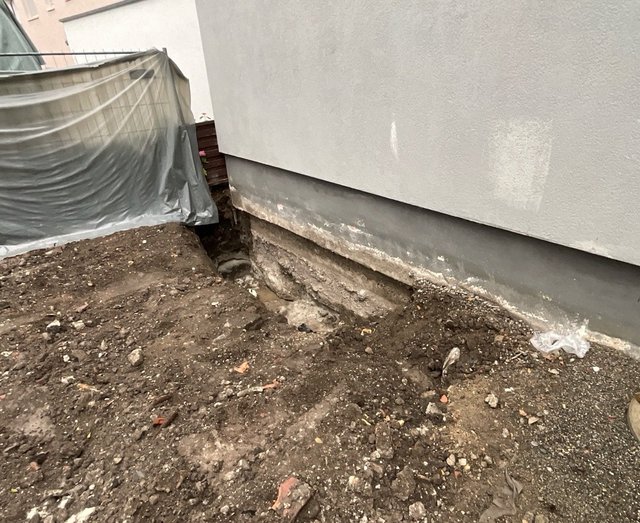 Freigelegte Fundamentwand mit offenem Erdaushub neben dem Gebäude