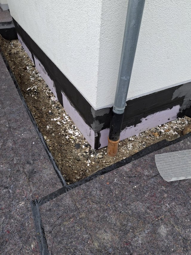 Schwarze Masse auf Sockelbereich an Gebäudeecke mit Fallrohr
