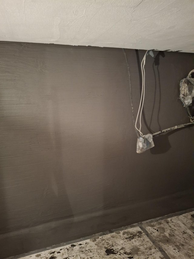 Dunkel beschichtete Kellerwand mit abgeklebten Kabeln, Boden mit Bauschmutz