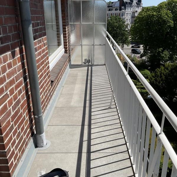 Langer Balkon mit Betonboden, Backsteinwand, Geländer und Sichtschutz aus Glasbausteinen