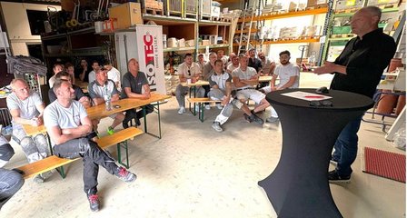 ISOTEC Mitarbeiter hält Vortrag vor sitzender Gruppe in Lagerhalle mit Regalen