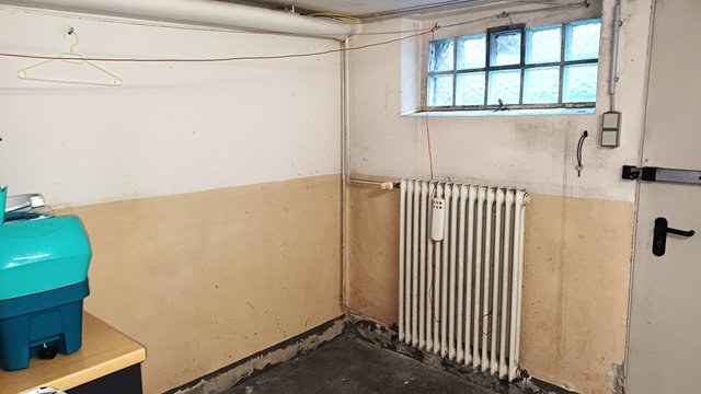 Abgenutzte Kellerwand mit Heizkörper und kleinen Wandspuren