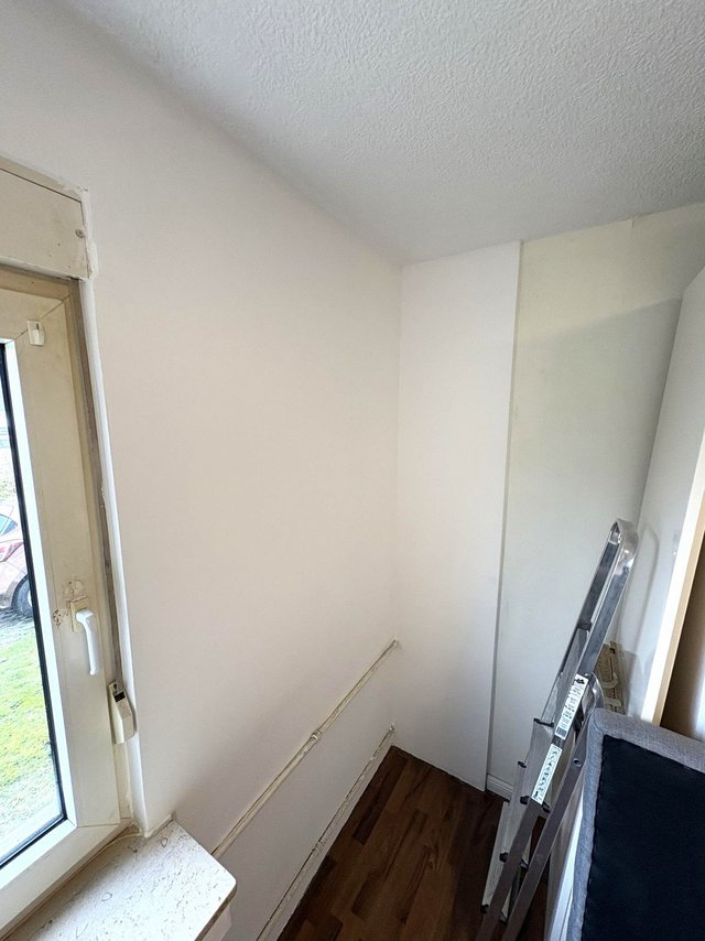 Leere Zimmerecke mit weißer Oberfläche, Fensterrahmen links und Leiter rechts.