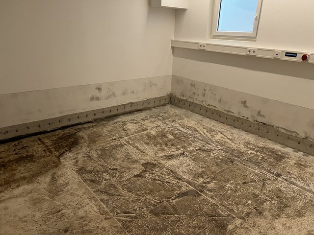 Freigelegter Boden und beschädigter Wandsockel in leerem Raum mit Feuchtigkeitsspuren