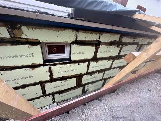 Helle Dämmplatten mit schwarzer Masse an Balkonwand, kleines Fenster mittig