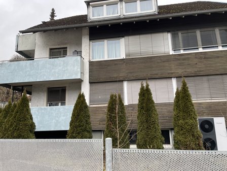 Mehrstöckiges Wohnhaus mit Balkonen, Holzfassade und Koniferen vor dem Gebäude
