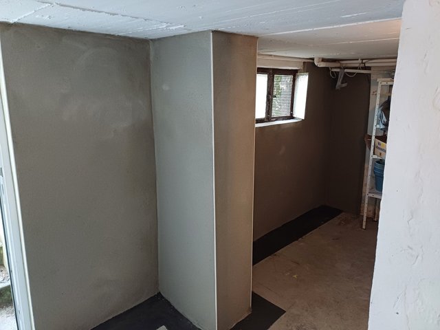 Frisch beschichtete Kellerwand mit grauer Masse und kleinem Fenster