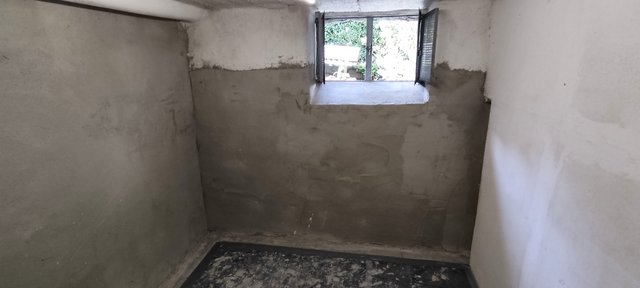 Kellerraum mit teils grauer Masse beschichteten Wänden und kleinem Fenster.