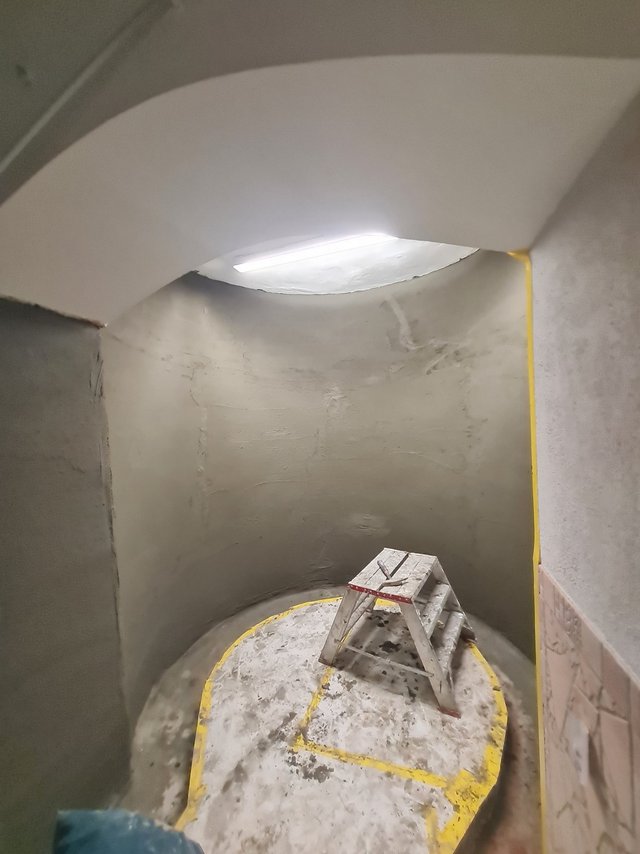 Graue Masse auf gewölbter Kellerwand, Leiter auf abgeklebtem Boden