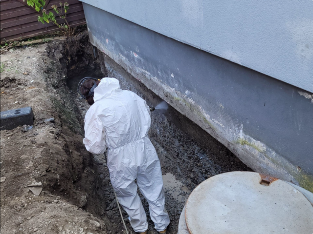 Arbeiter sprüht transparente Flüssigkeit auf freigelegte Hauswand