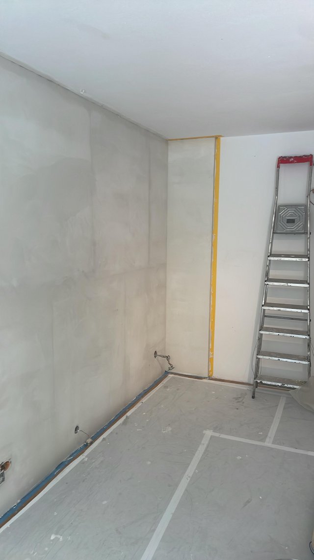 Abgedeckter Raum mit gespachtelter Wandfläche, Leiter an weißer Wand.