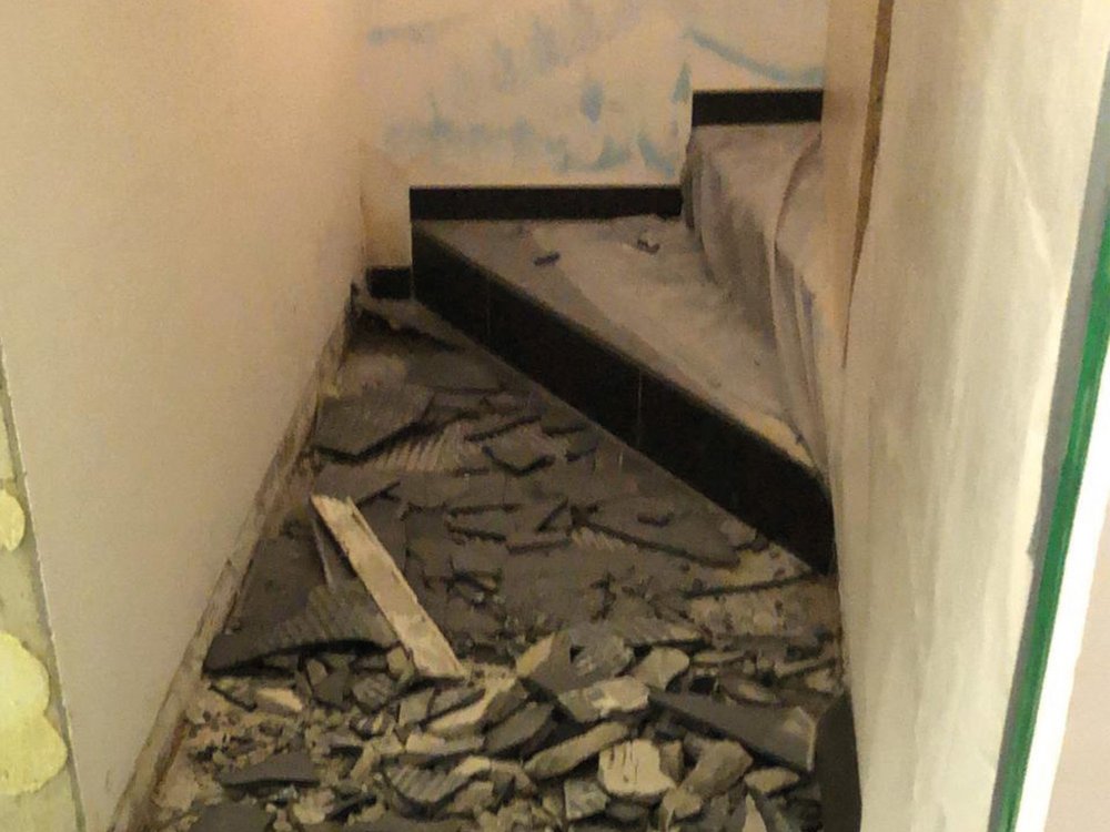Flur mit aufgebrochenen dunklen Bodenfliesen und Bauschutt, Sanierungsarbeiten