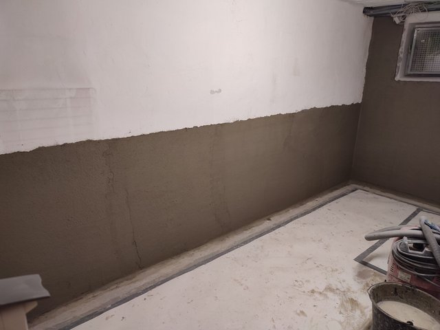 Unfertige Kellerwand mit weißer Fläche oben und grauer Masse unten, Baustellenecke mit Werkzeugen.