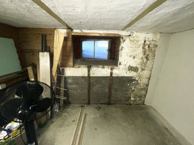 Kellerraum mit kleinem Fenster und fleckiger, abplatzender Wandoberfläche.