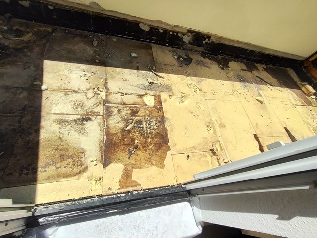 Verschmutzter Balkonboden mit abgelösten Platten und dunklen Rückständen