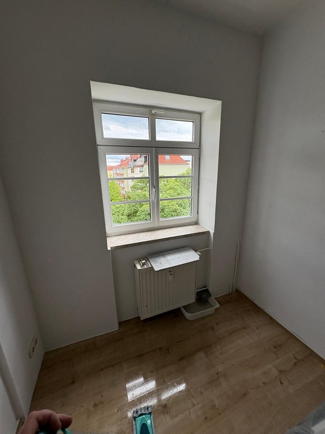 Leerer Raum mit Fenster, Heizkoerper und Holzfussboden, Blick auf Haeuser und Baeume.