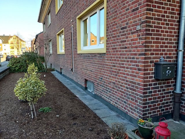 Ziegelhaus mit Vorgarten, Gehweg und Kellerfenstern an der Seitenfassade