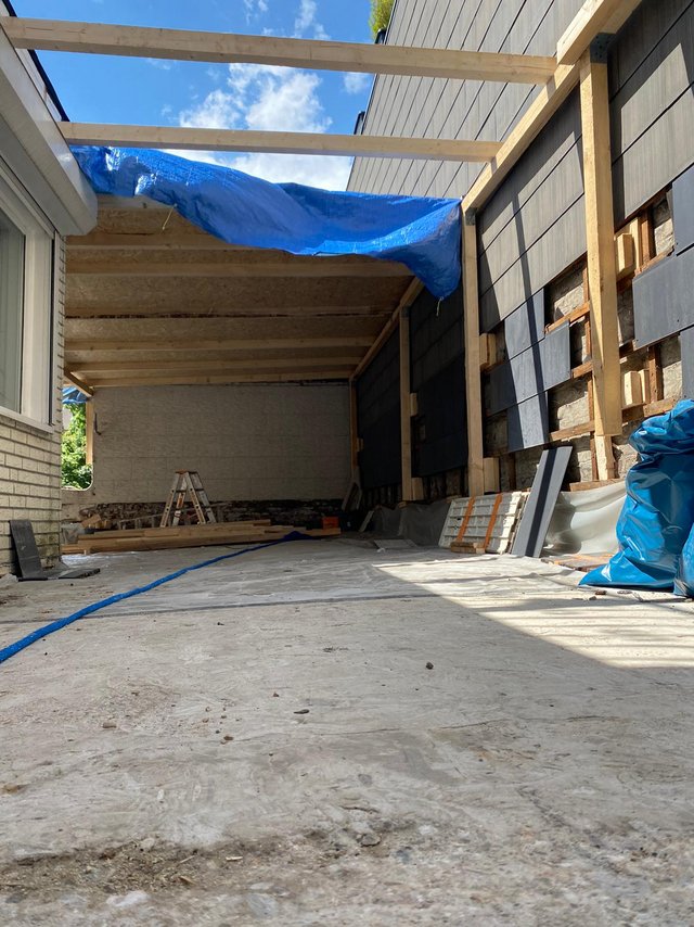 Baustelle mit Holzbalken, schwarzer Fassadenverkleidung und freiliegender Steinwand