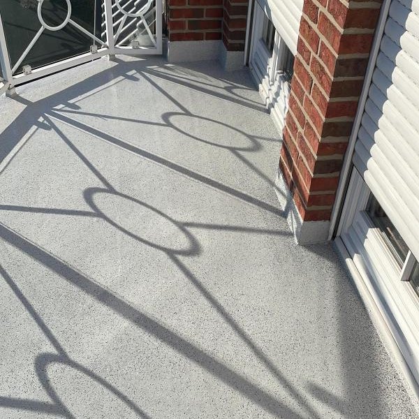 Balkon mit hellem Bodenbelag, Backsteinpfeilern und Geländerschatten