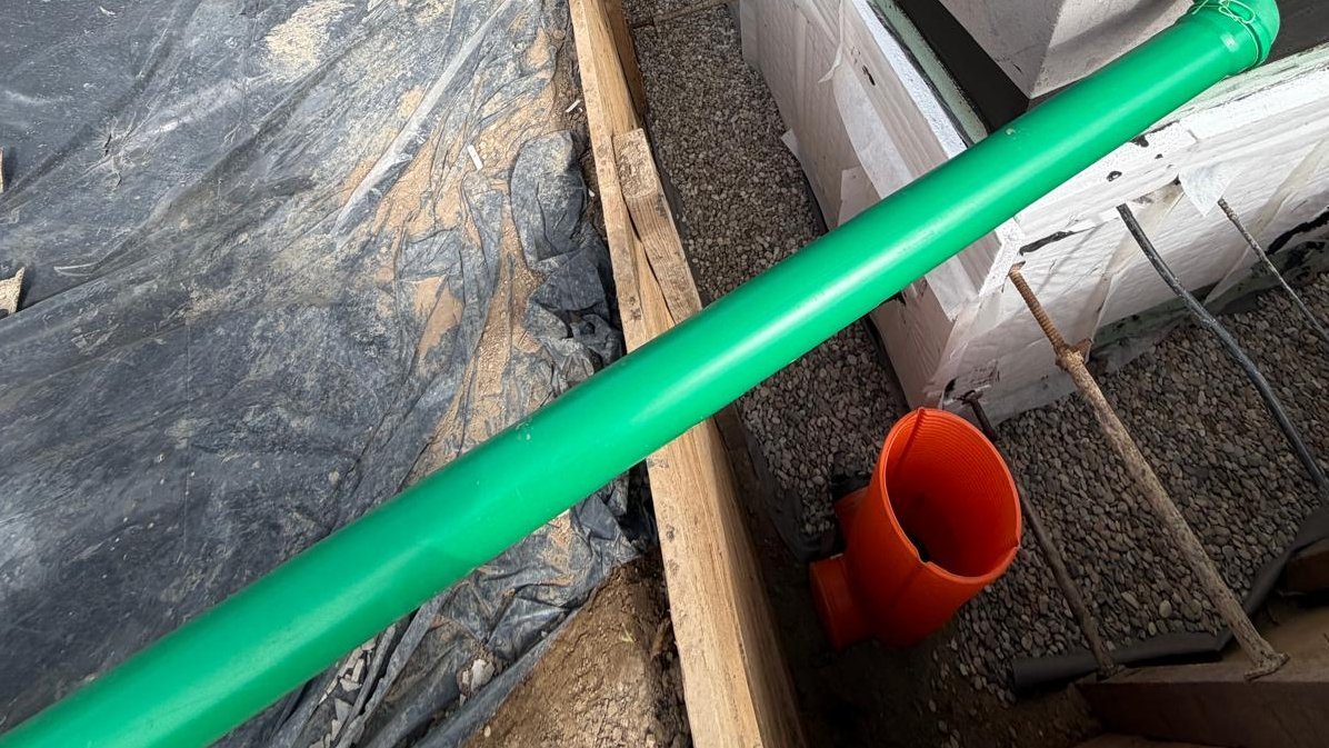 Freigelegte Kellerwand mit Schutzfolie, Kiesbett und orangefarbenen Drainagerohren