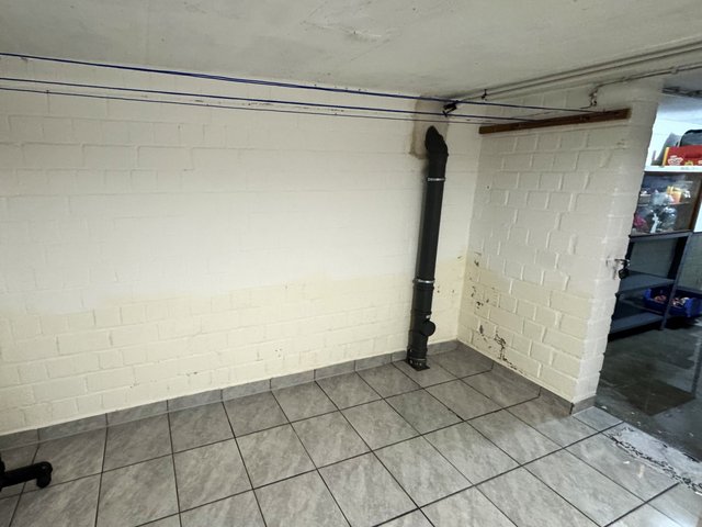 Weiß gestrichene Kellerwand mit schwarzem Rohr und Flecken im unteren Eck