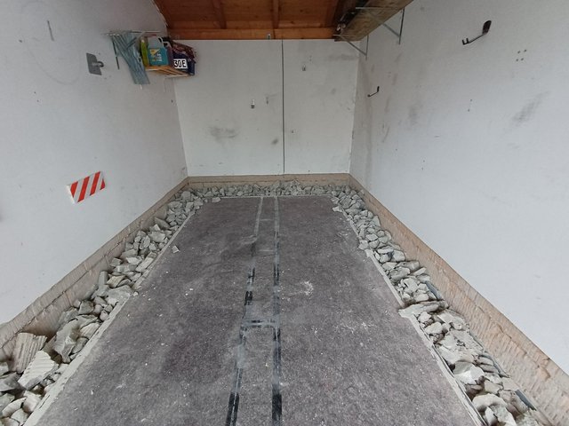 Aufgestemmter Bodenrand mit Bauschutt entlang der Wände in leerem Raum