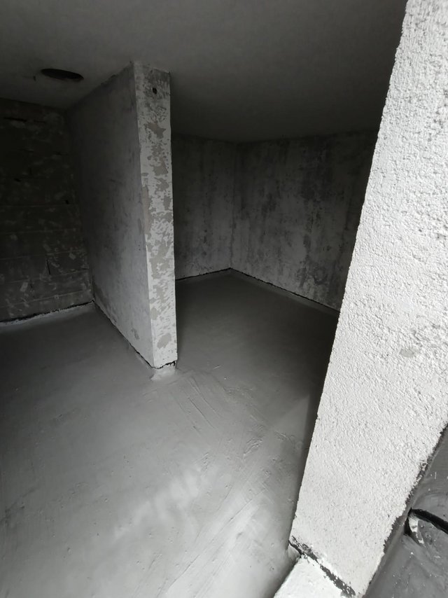 Grauer Bodenbelag in Rohbaukeller, Betonwände mit dunklen Feuchtespuren.