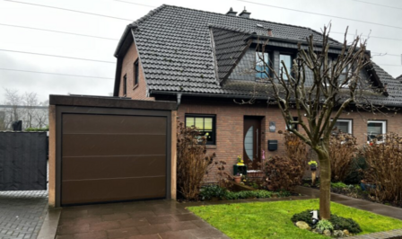 Einfamilienhaus mit Garage, Vorgarten und kahlem Baum an regnerischem Tag