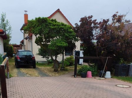 Gepflasterte Hofeinfahrt mit geparktem Auto, Bäumen, Mülltonnen und Haus im Hintergrund