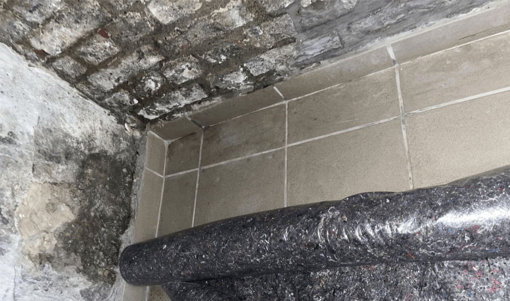 Dunkle Flecken an Kellerdecke und -ecke neben beige gefliester Fläche, Nahaufnahme